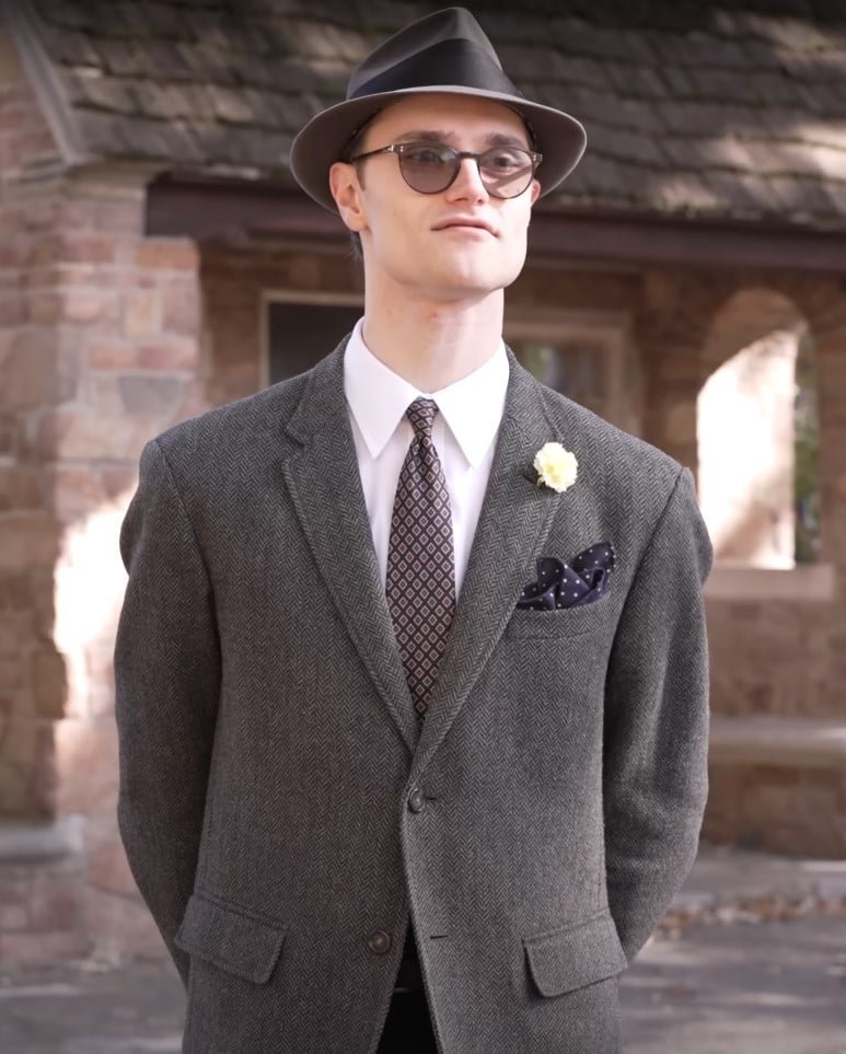 Veste gris à chevrons fedora Square de poche Preston en veste à chevrons gris avec une cravate à motifs, un carré de poche à polka marine, une boutonnie jaune et un chapeau Fedora.