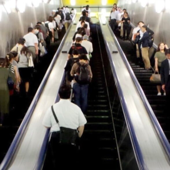 Le banlieue se tenant sur le côté gauche d'un long escalator au Japon.