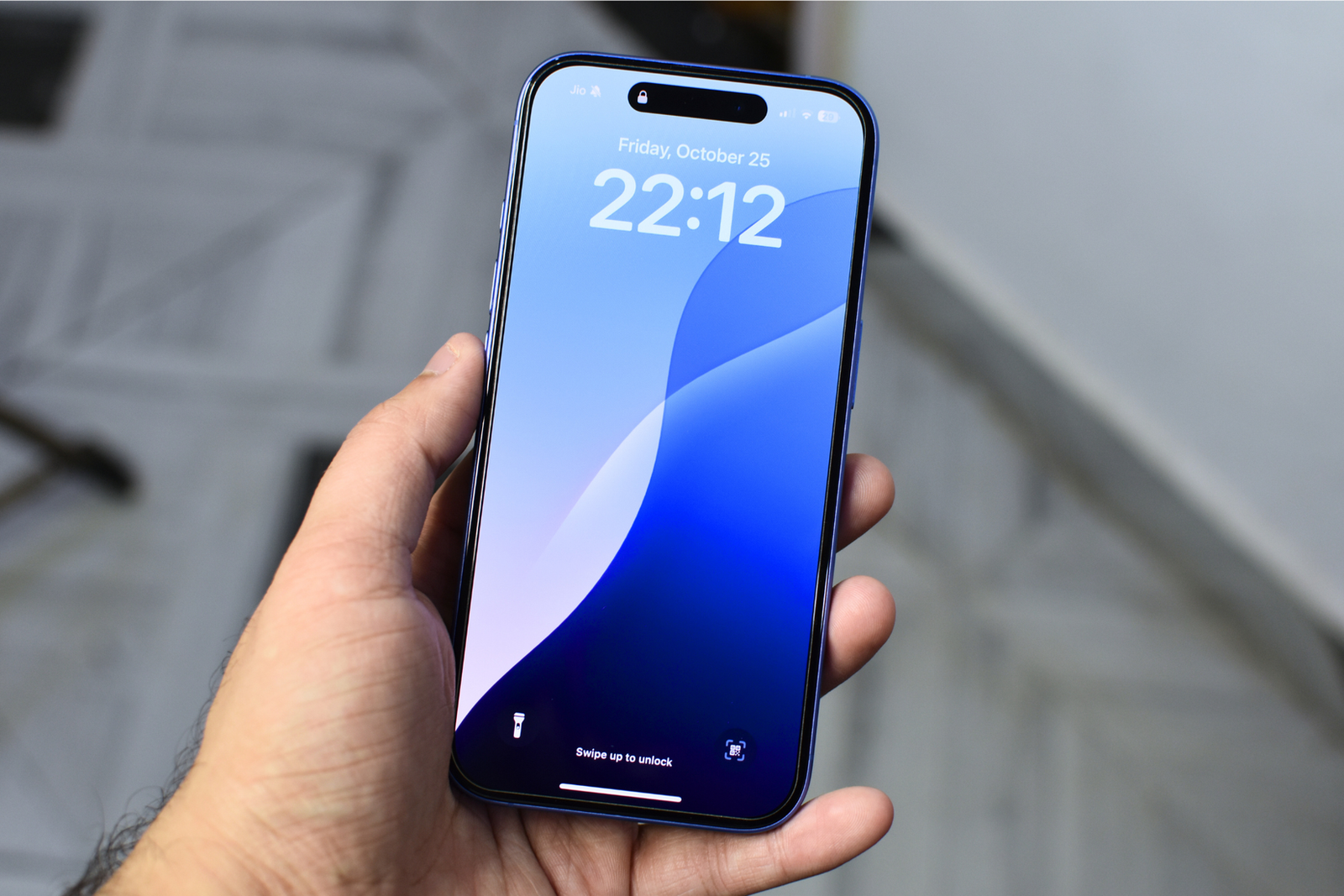 L'iPhone 16 tenu en main avec l'écran montrant le papier peint de l'écran de verrouillage de couleur bleue.