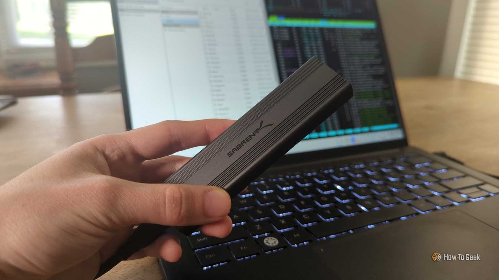La main d'une personne tenant un lecteur SSD externe sabrent devant un ordinateur portable Linux.