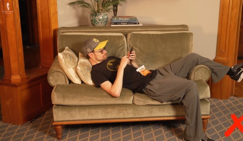 Se prélasser sur le canapé L'homme se prélasse sur le canapé avec des jambes largement répandues et en utilisant le téléphone