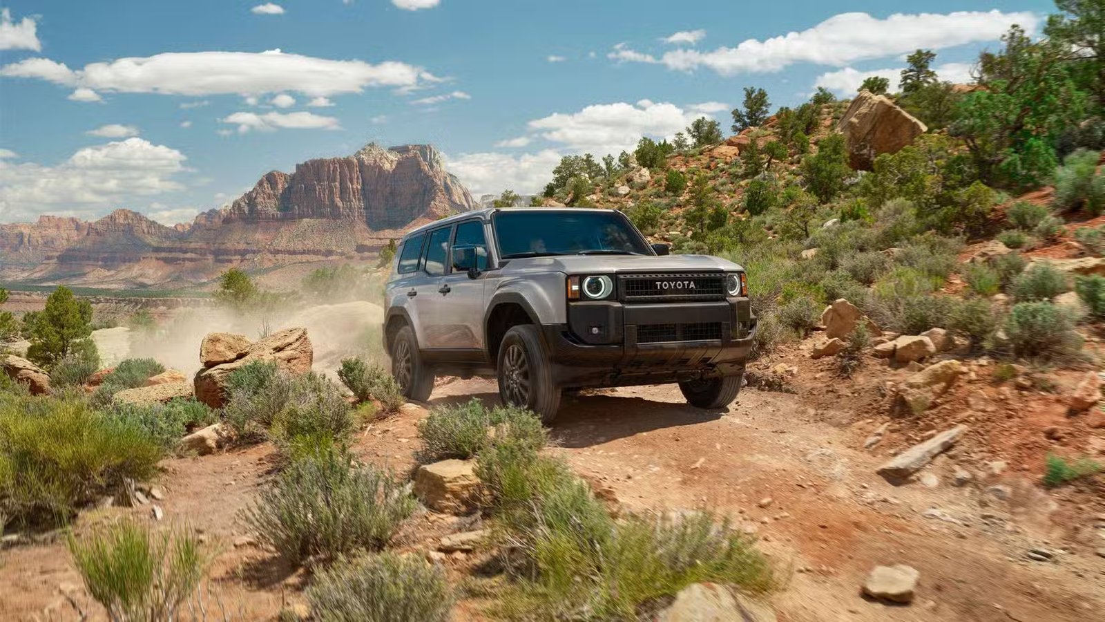 Friont 3/4 View of a Silver 2025 Toyota Land Cruiser hors route dans le désert avec des montagnes en arrière-plan.