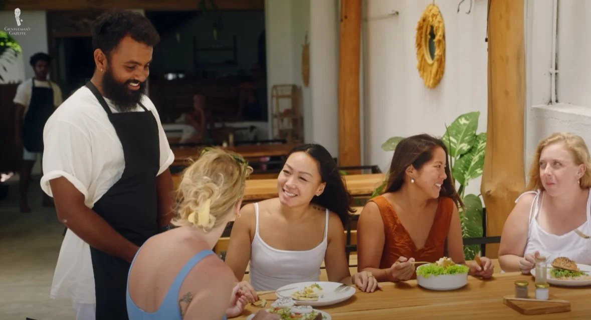 Un chef souriant dans un tablier engageant chaleureusement avec un groupe de convives dans un restaurant en plein air.