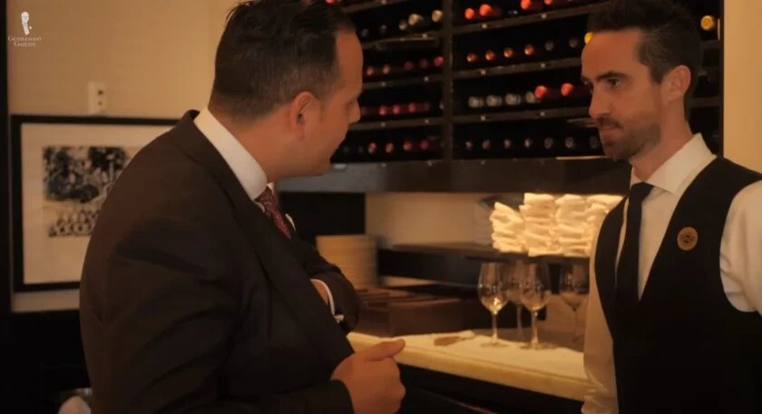 Un gentleman dans un costume en parlant discrètement avec un sommelier dans un restaurant pour gérer le paiement d'un repas.