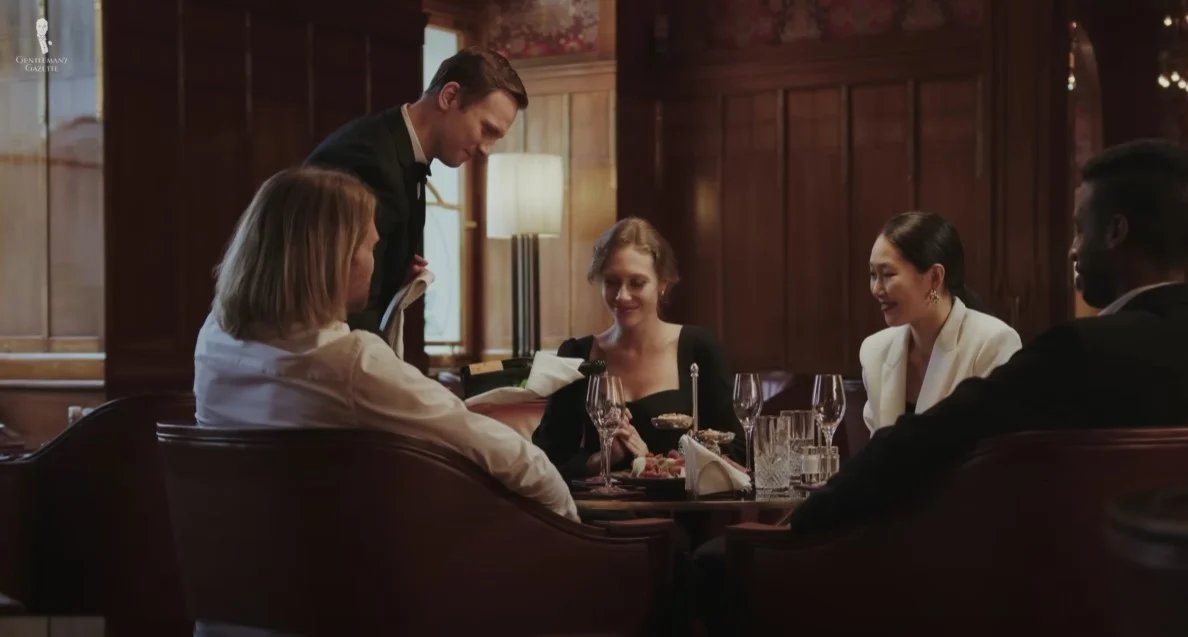 Une femme à une table de restaurant parlant positivement à un serveur féminin tenant une bouteille d'eau.