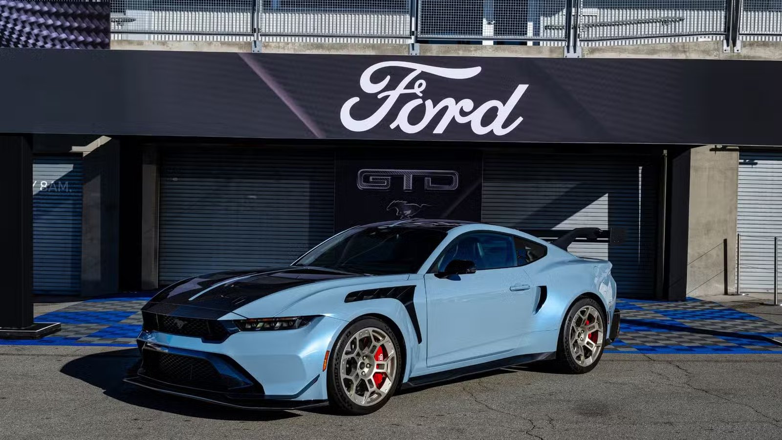 Vue de trois quarts avant d'une Mustang GTD 2025 bleue garée dans la voie des stands avec un panneau Ford au-dessus.