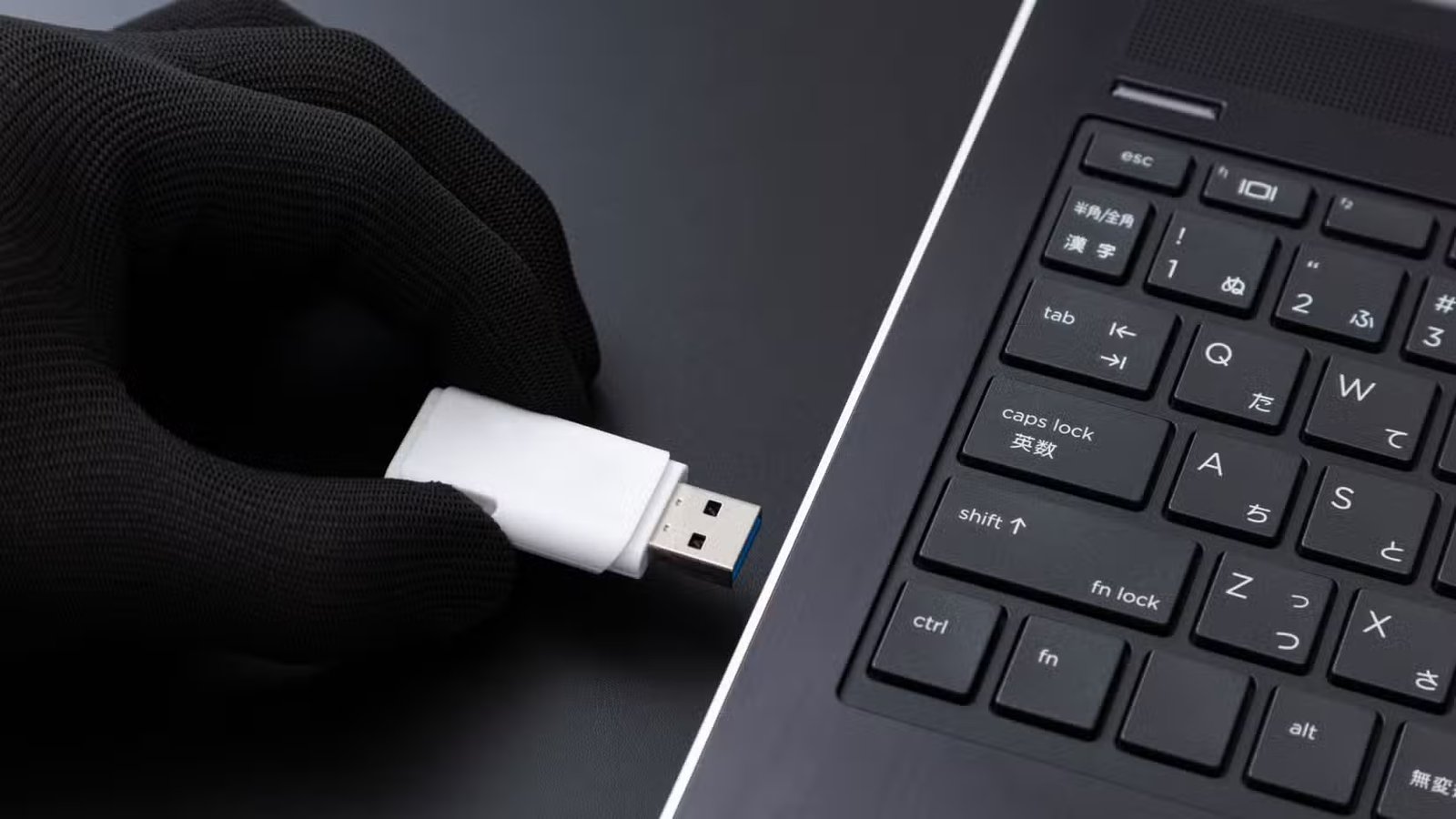 Une main gantée insère une clé USB dans un ordinateur portable.