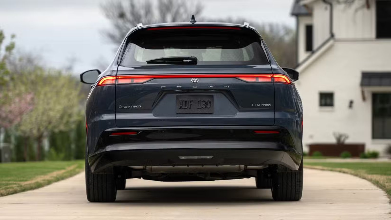 Plan arrière statique d'une Toyota Crown Signia Limited 2025 grise garée dans l'allée d'une maison.