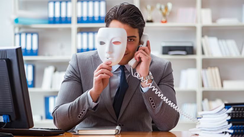 Un homme d'affaires dans un bureau qui passe un appel téléphonique et qui regarde derrière un masque facial.