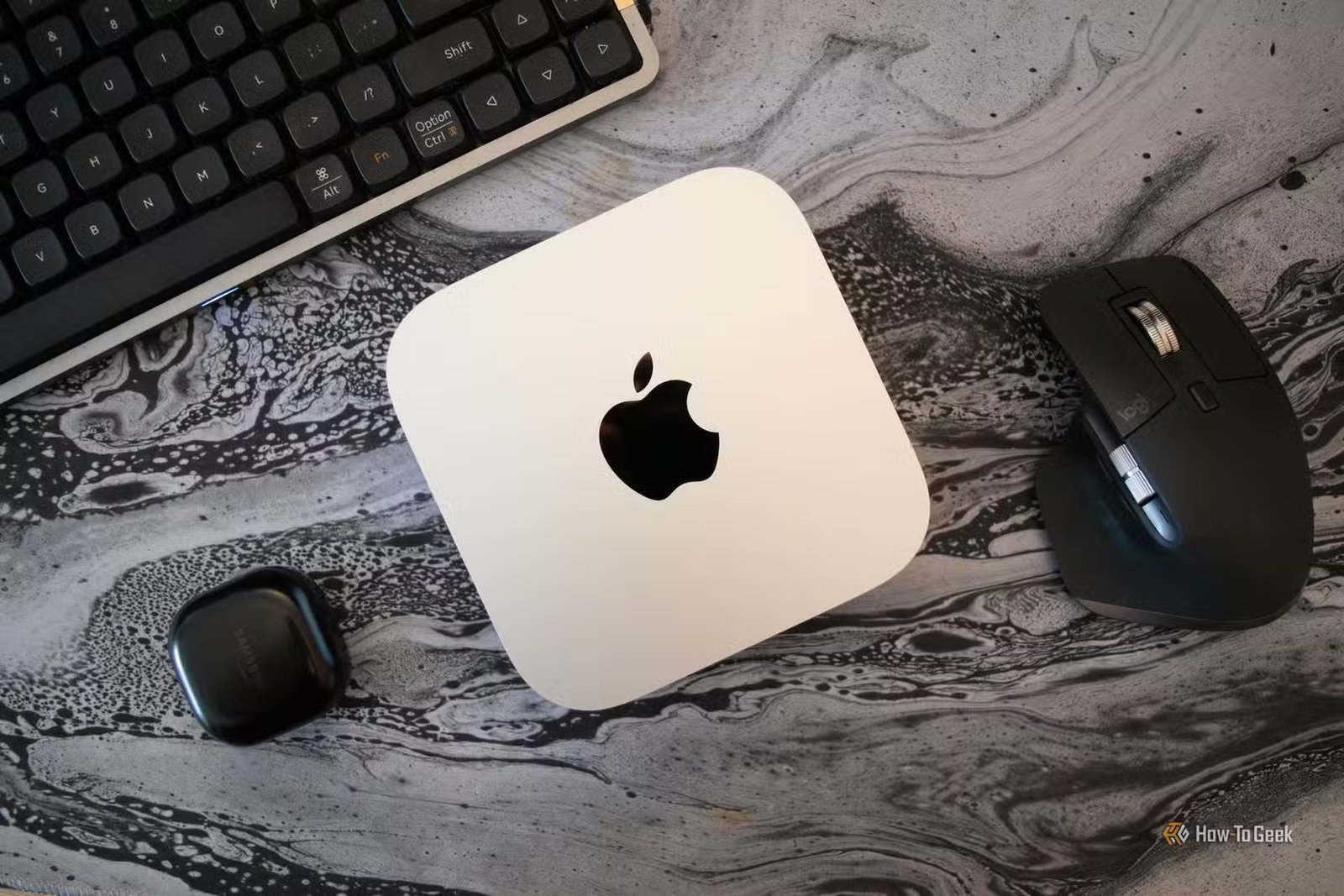 Un Mac Mini M4 posé sur un bureau entouré de divers périphériques PC. 