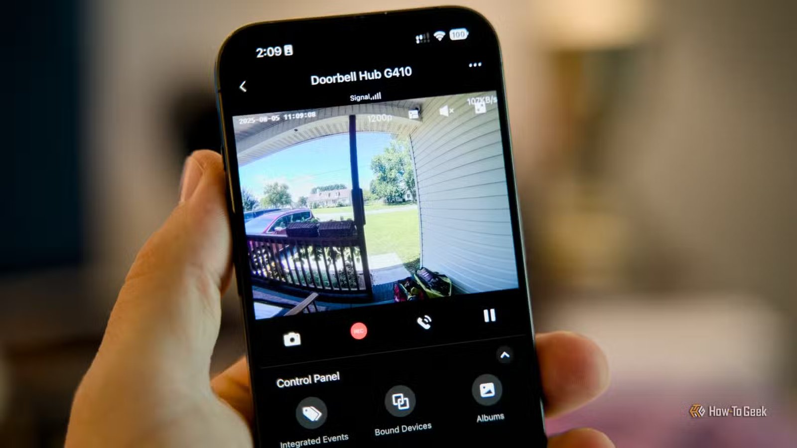 Une main tenant un iPhone avec l'application Aqara ouverte montrant le flux vidéo du hub Doorbell G410.