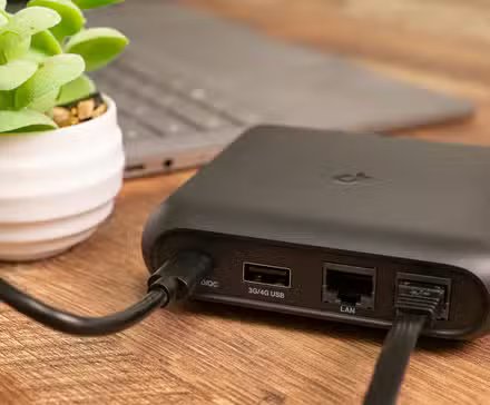 Un routeur de voyage à côté d’un ordinateur portable et d’une petite plante. 