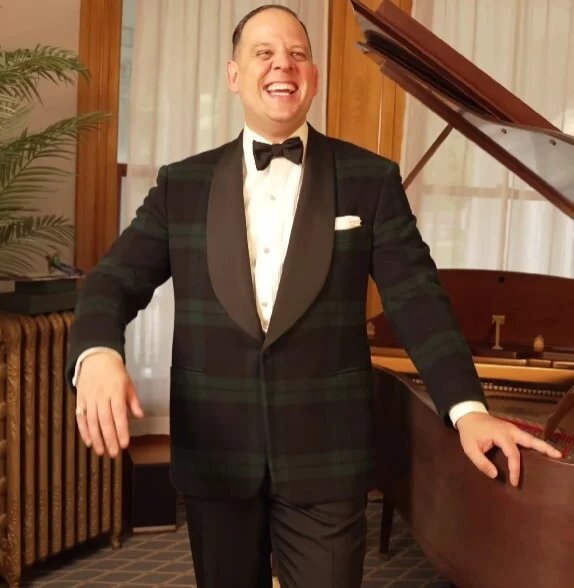Raphael Schneider debout près d'un piano portant une veste de soirée en tartan Ralph Lauren Purple Label Black Watch avec un col châle.