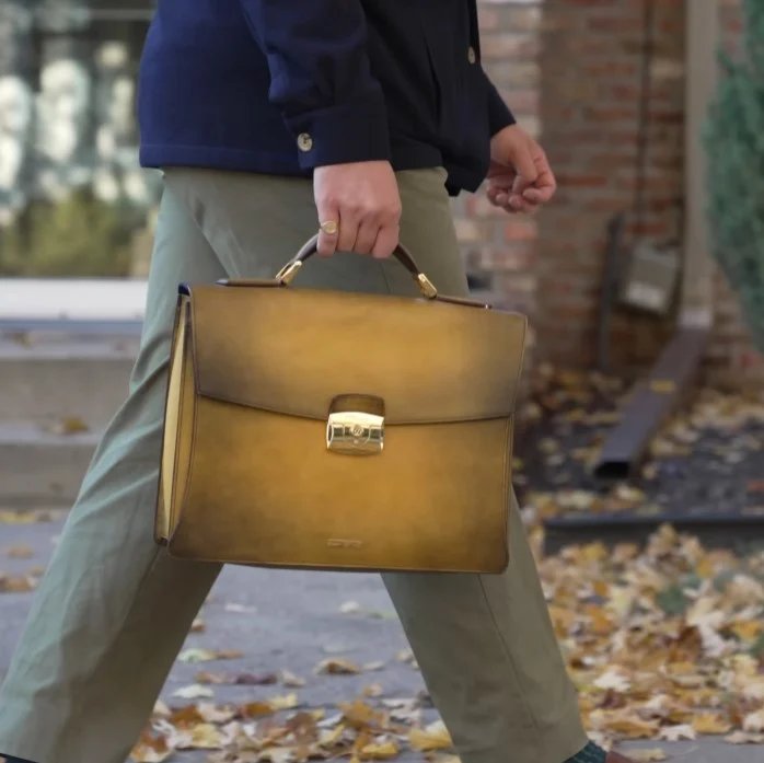 Une mallette vintage en cuir ST Dupont avec une patine jaunâtre unique et une serrure en laiton plaqué or portée par un homme en pantalon vert.
