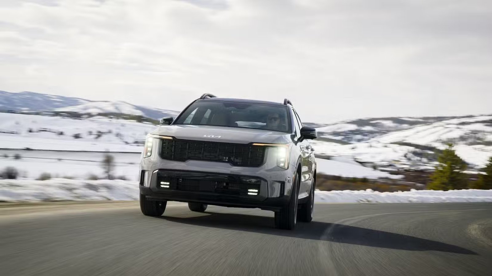Prise de vue dynamique de l'avant d'un Kia Sorento 2026 roulant sur une route de campagne enneigée.
