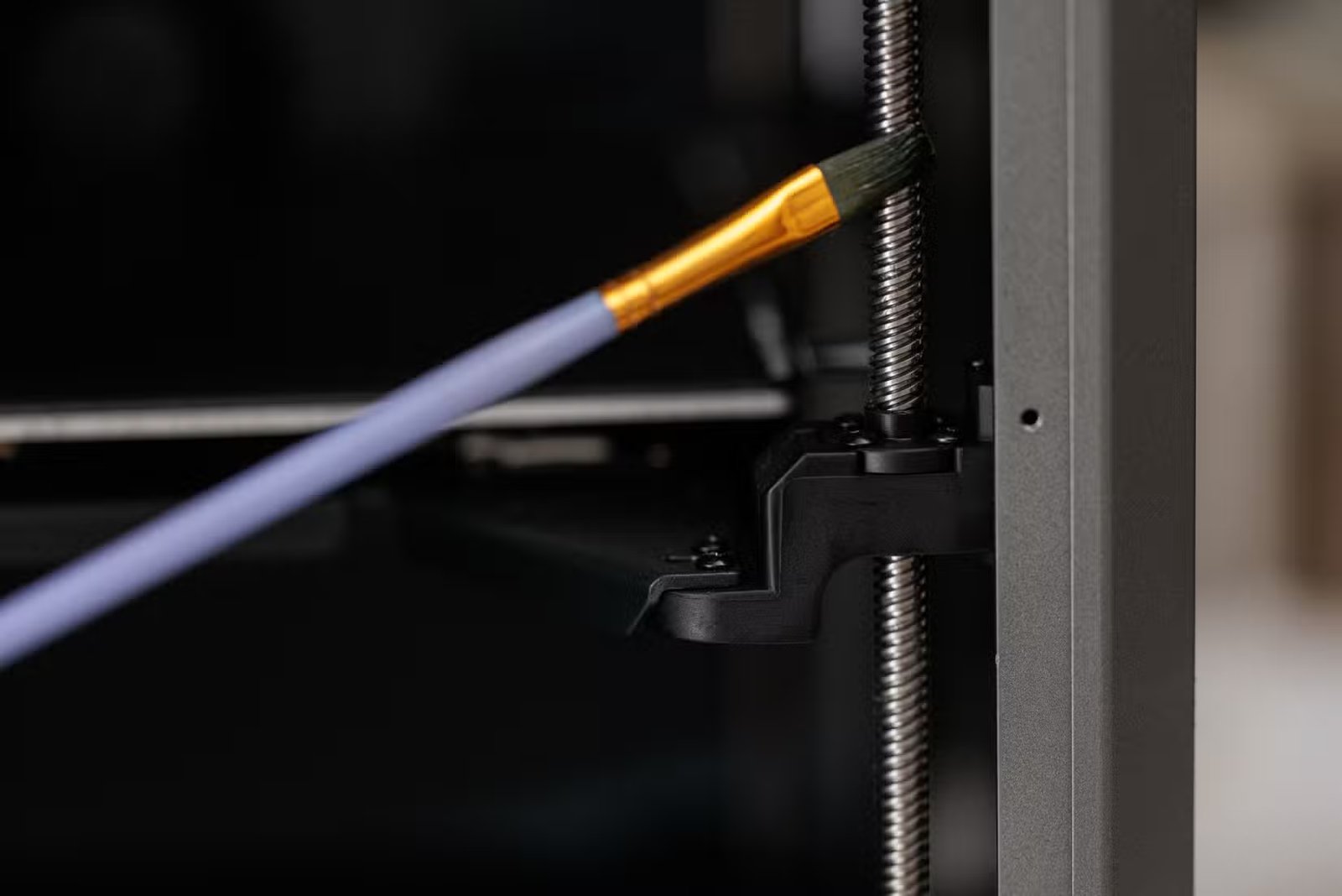 Application de lubrifiant au pinceau sur la tige filetée à l'intérieur d'une imprimante 3D.