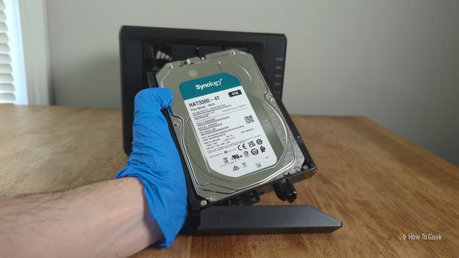 Main gantée d'une personne tenant un disque dur Synology devant le NAS Synology DS425+.-2