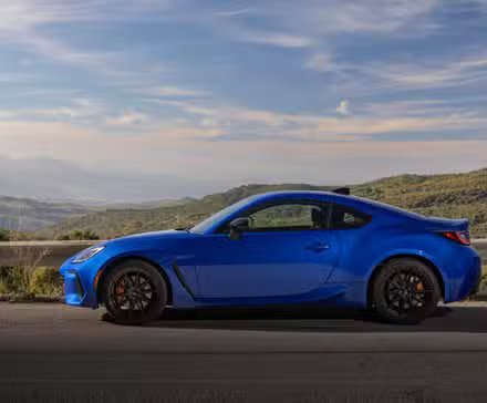 Photo de profil latérale statique d'une Subaru BRZ tS 2024 bleue avec des montagnes et des arbres en arrière-plan.