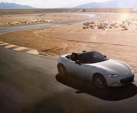 Plan dynamique 3/4 avant d'une Mazda MX-5 2024 argentée sur une piste de course dans le désert.