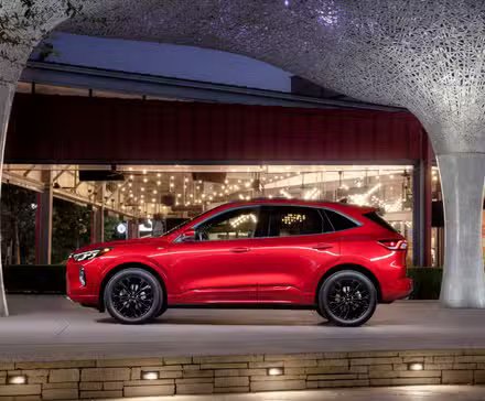 Photo de profil latérale statique d'un Ford Escape ST-Line Elite 2023 rouge garé à l'extérieur d'un bâtiment moderne.