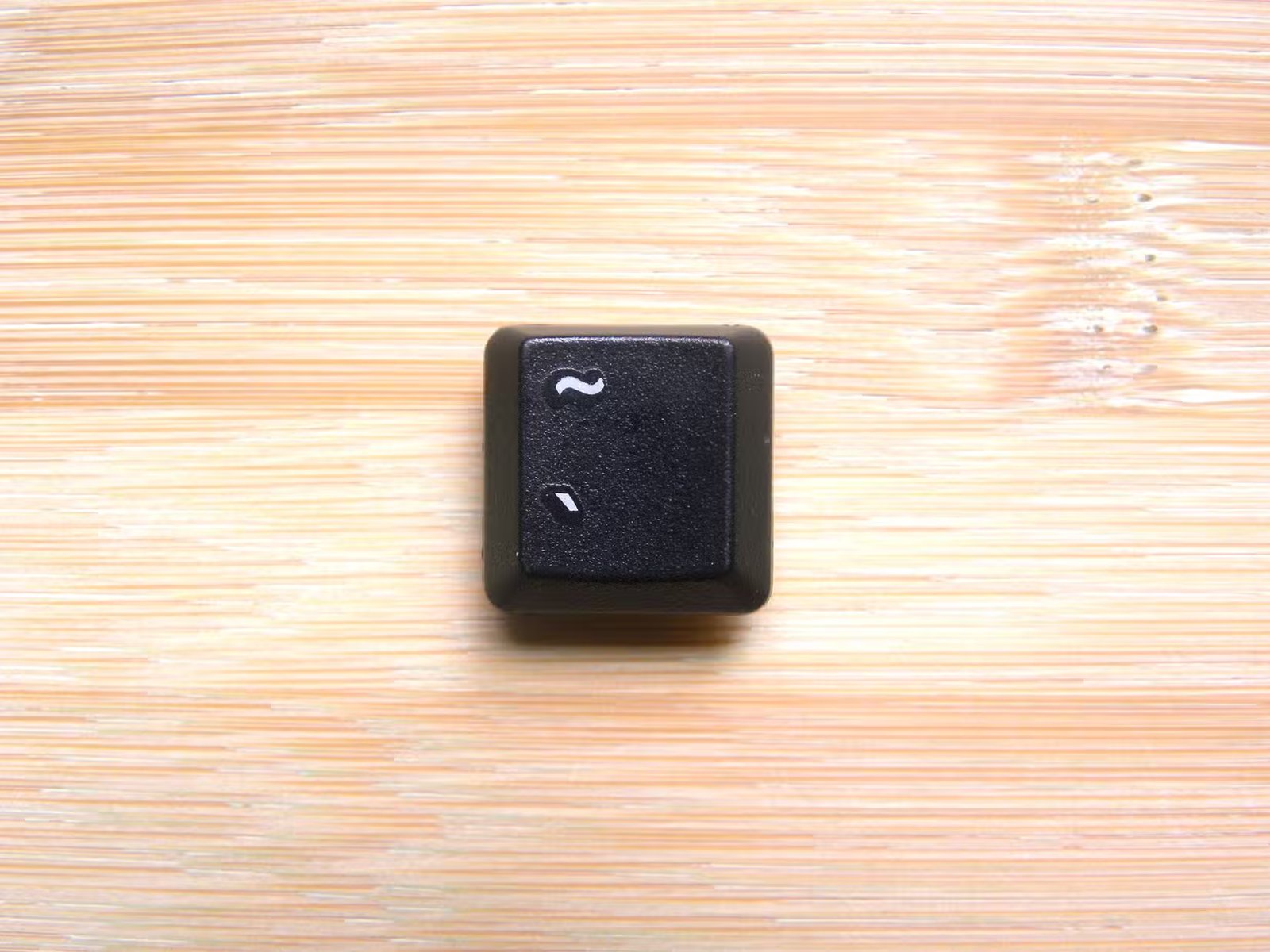 Une touche tilde de clavier sur fond de bois