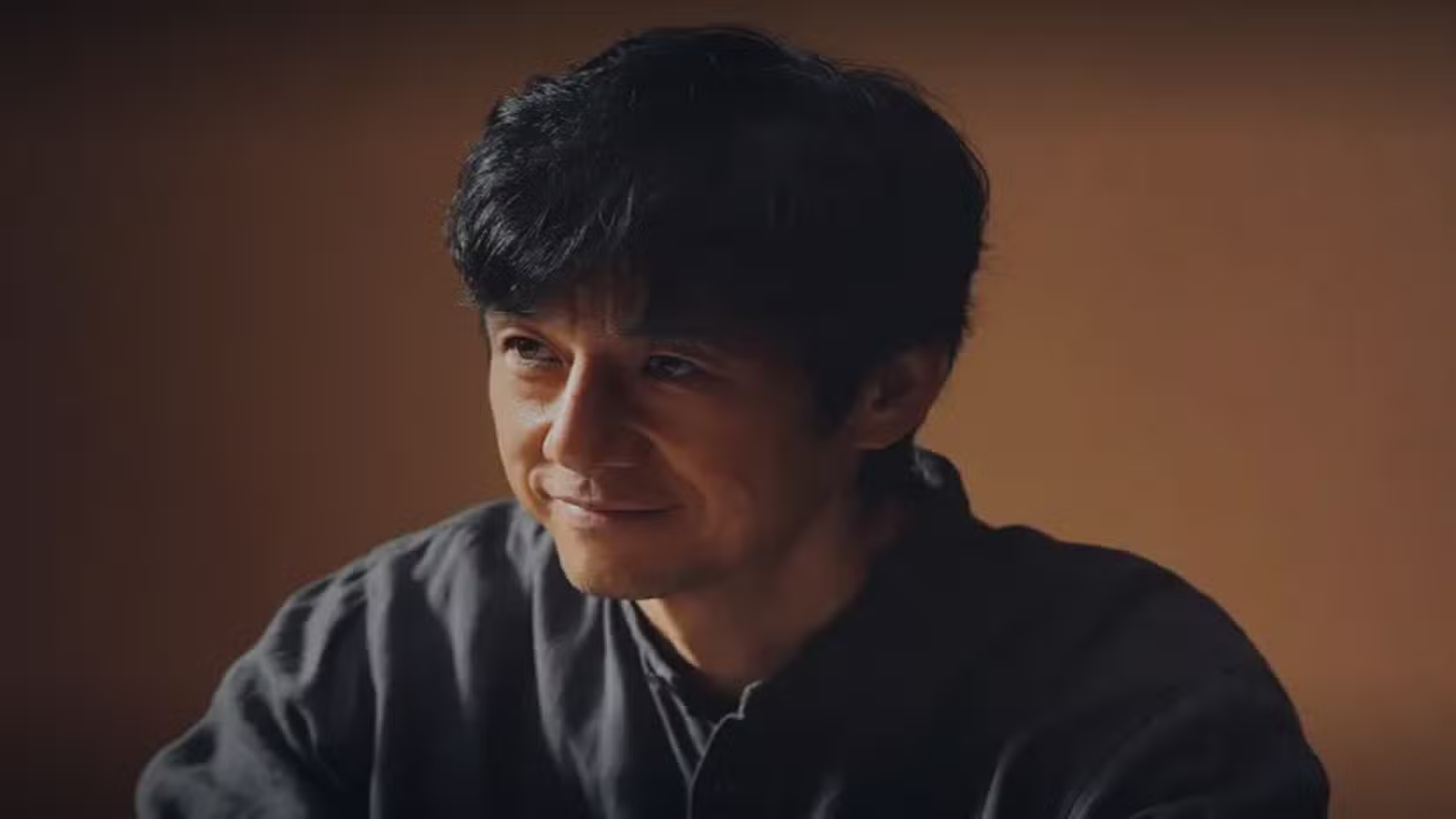 Capture d'écran de Nishijima Hidetoshi de Human Specimens, vêtu d'une chemise grise et souriant.