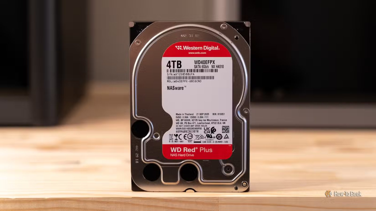 Un disque dur NAS Western Digital WD Red Plus de 4 To posé sur un bureau en bois avec des imprimantes 3D en arrière-plan.