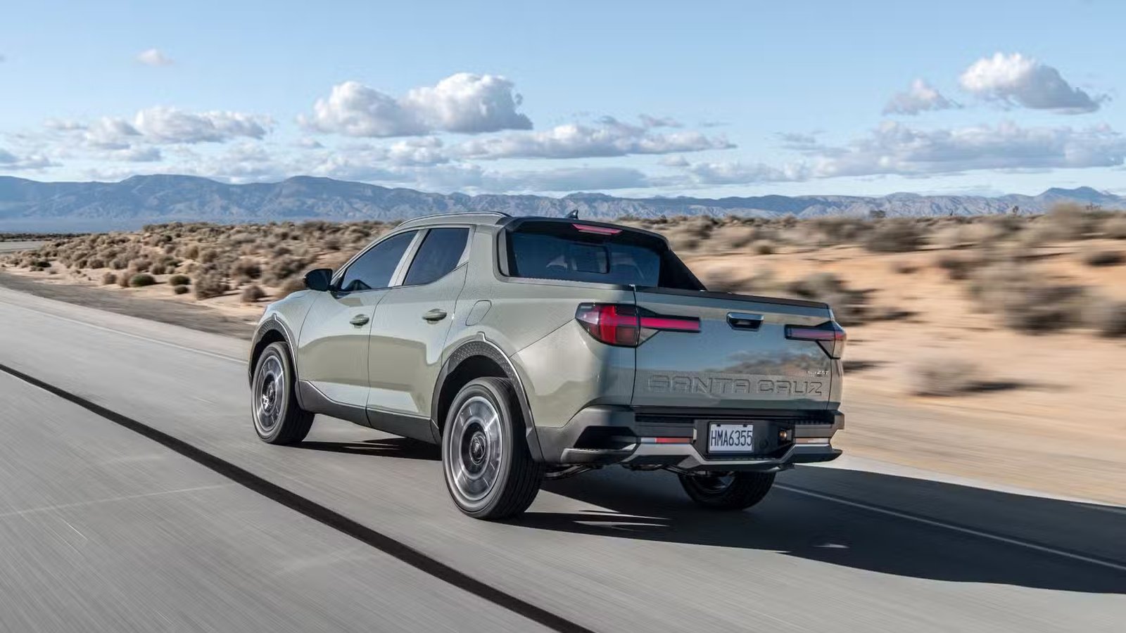Plan 3/4 arrière dynamique d'une Hyundai Santa Cruz Limited 2025 verte roulant sur une route à travers le désert.