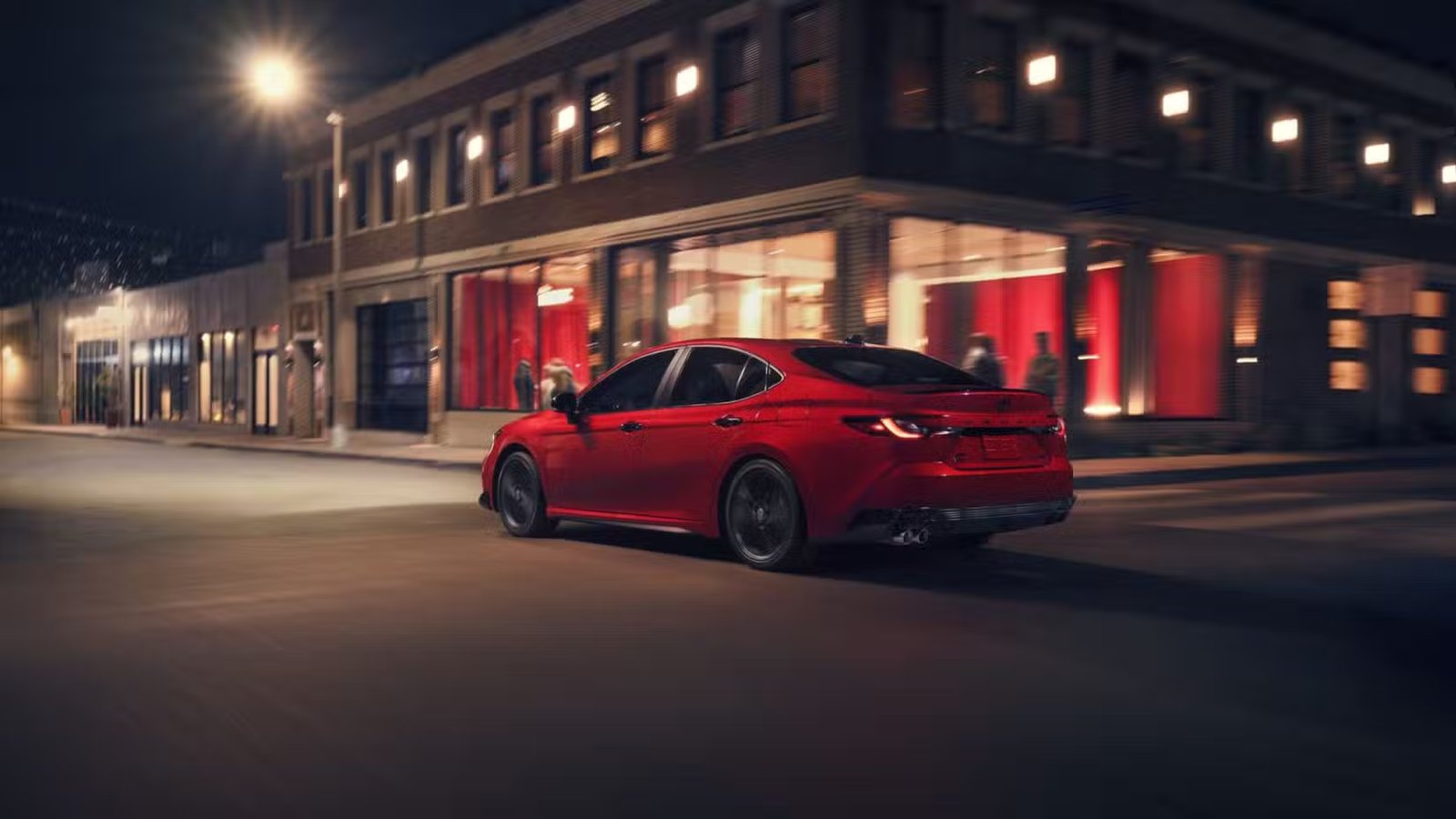 Plan dynamique 3/4 arrière d'une Toyota Camry Nightshade 2026 rouge traversant une ville.