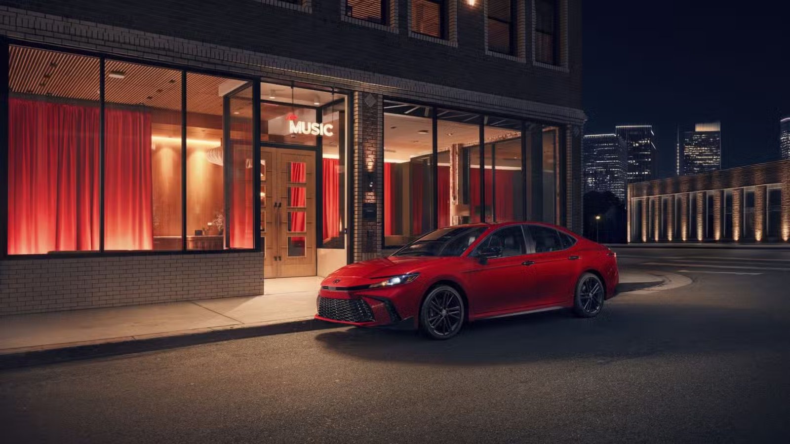Plan statique 3/4 avant d'une Toyota Camry Nightshade 2026 rouge garée à l'extérieur d'un bâtiment.