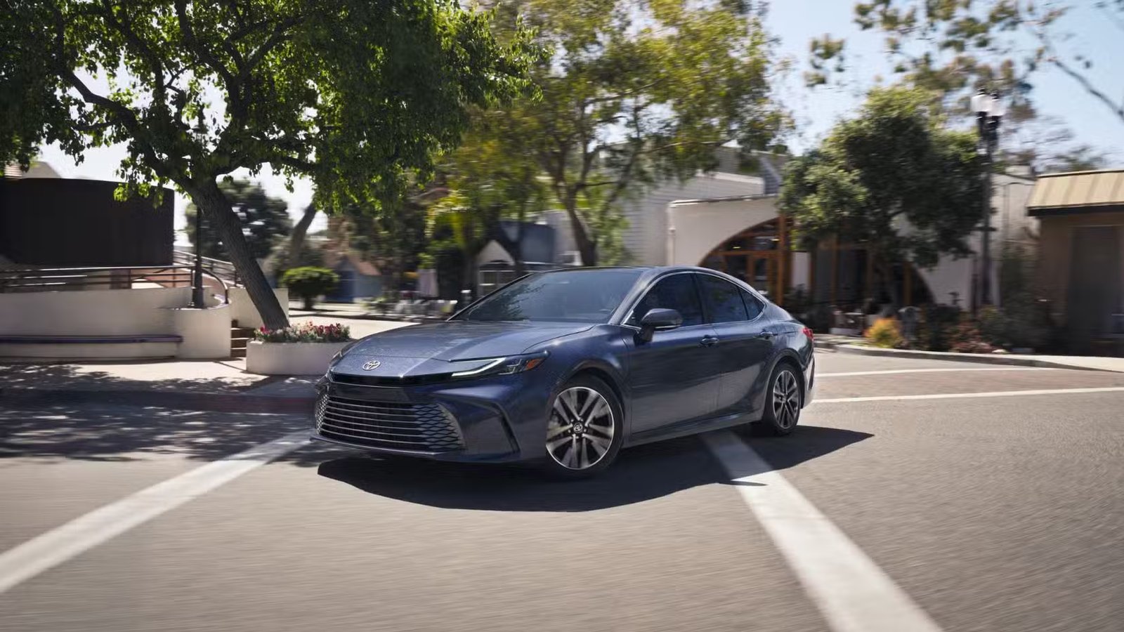 Plan dynamique 3/4 avant d'une Toyota Camry 2026 grise traversant une ville.