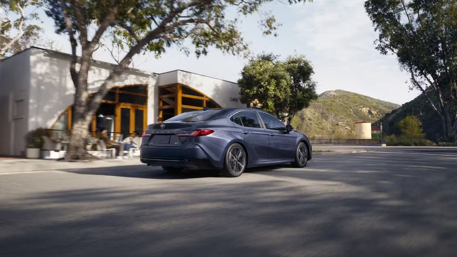 Plan dynamique 3/4 arrière d'une Toyota Camry 2026 grise traversant une ville.