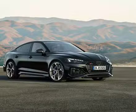 Vue complète d'une Audi RS5 Sportback noire garée sur le tarmac avec des montagnes en arrière-plan.
