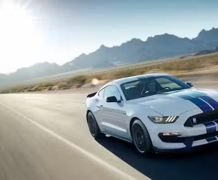 Vue 3/4 avant d'une Ford Mustang Shelby GT350 2017 blanche roulant sur une route de campagne avec des montagnes en arrière-plan.