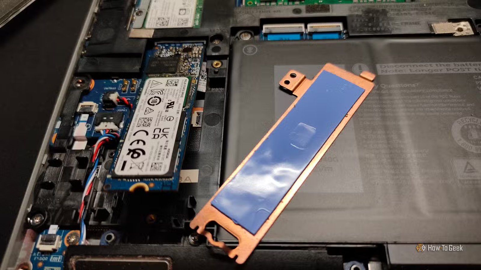 Un dissipateur thermique NVMe en cuivre avec des coussinets thermiques à côté d'un SSD NVMe à l'intérieur d'un ordinateur portable.