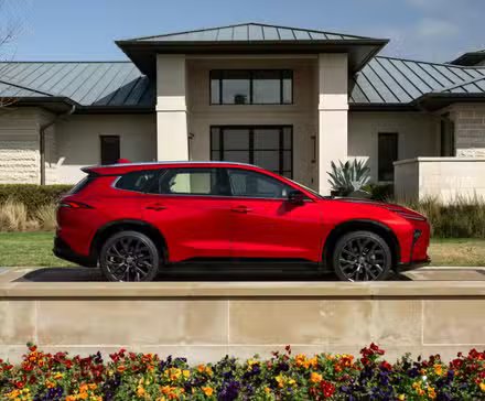 Photo de profil latérale statique d'une Toyota Crown Signia Limited 2025 rouge garée à l'extérieur d'une maison.