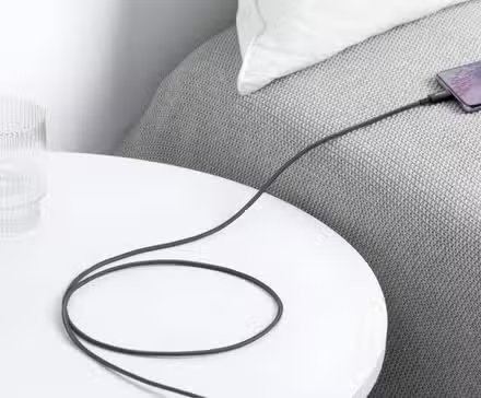 Le câble Anker USB C vers USB C était suspendu au-dessus d'une table de nuit à côté d'un lit, chargeant un téléphone.