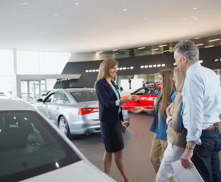 Vendeur dans la salle d'exposition d'un concessionnaire remettant à une famille les clés d'une nouvelle voiture.