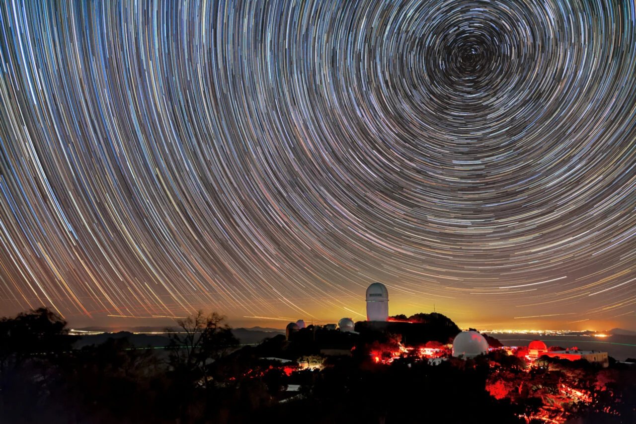 Cercles de lumière sur le ciel nocturne. Un dôme de télescope au sommet d’une montagne se trouve en dessous du centre du cercle.