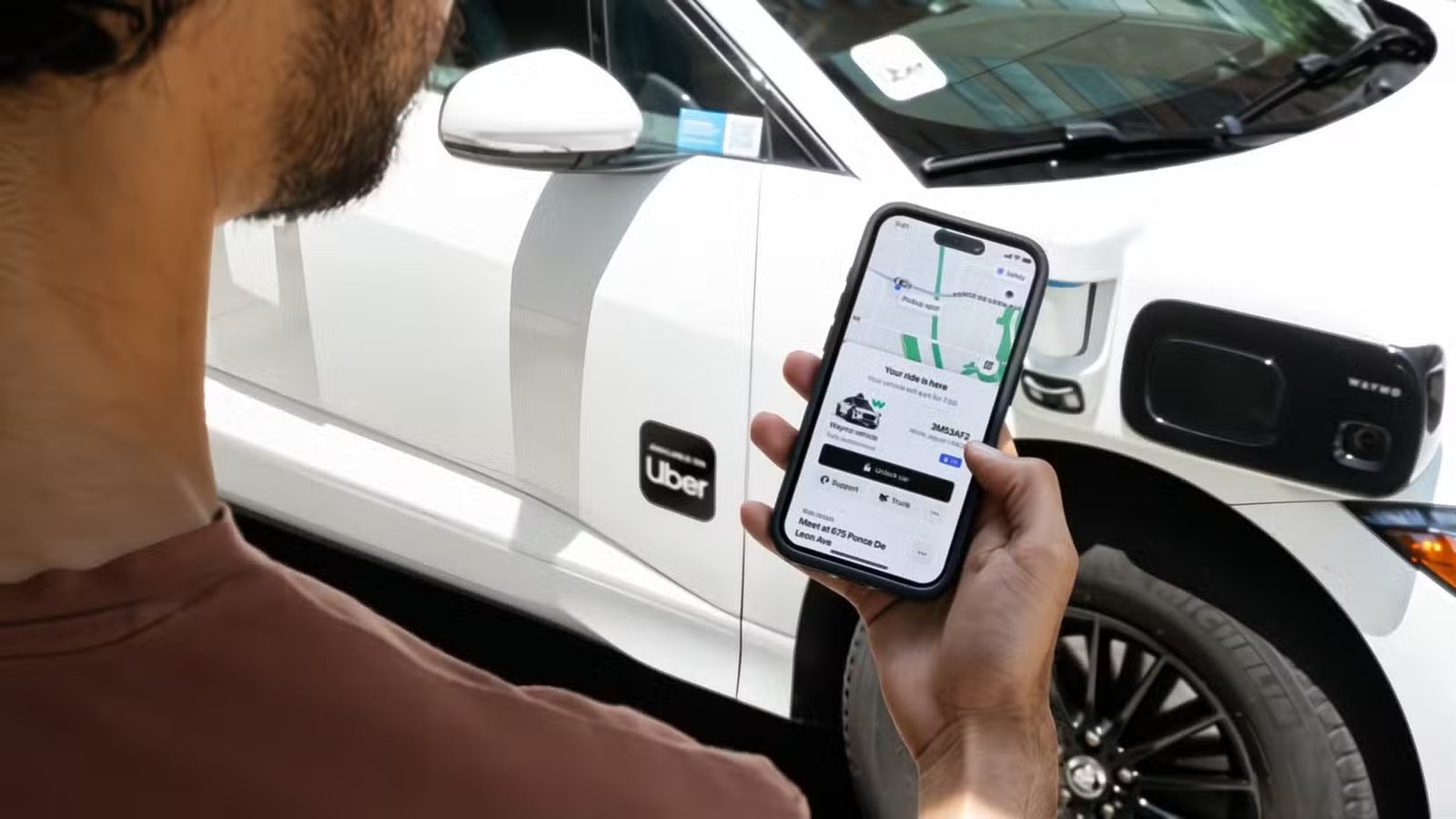 Un homme regardant son application Uber à côté d'une voiture portant le logo Uber.