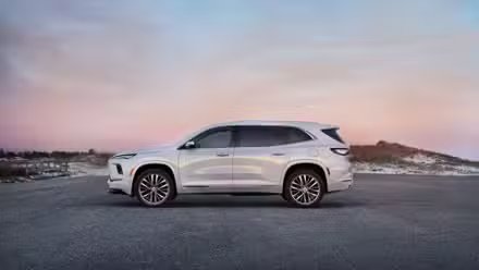 Photo de profil latérale statique d'une Buick Enclave Avenir 2025 blanche garée sur le tarmac.