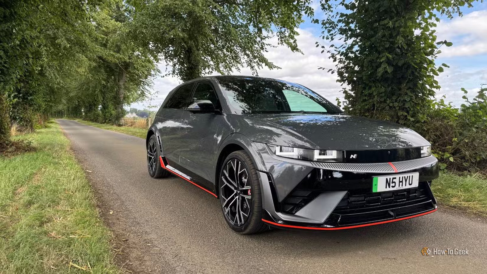 Plan statique 3/4 avant d'une Hyundai Ioniq 5 N 2025 grise garée sur une route de campagne bordée d'arbres.