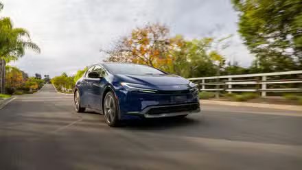 Vue 3/4 avant d'une Toyota Prius 2025 bleu marine roulant sur une route de campagne.