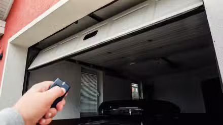 Une main tenant un porte-clés ouvrant une porte de garage à distance.