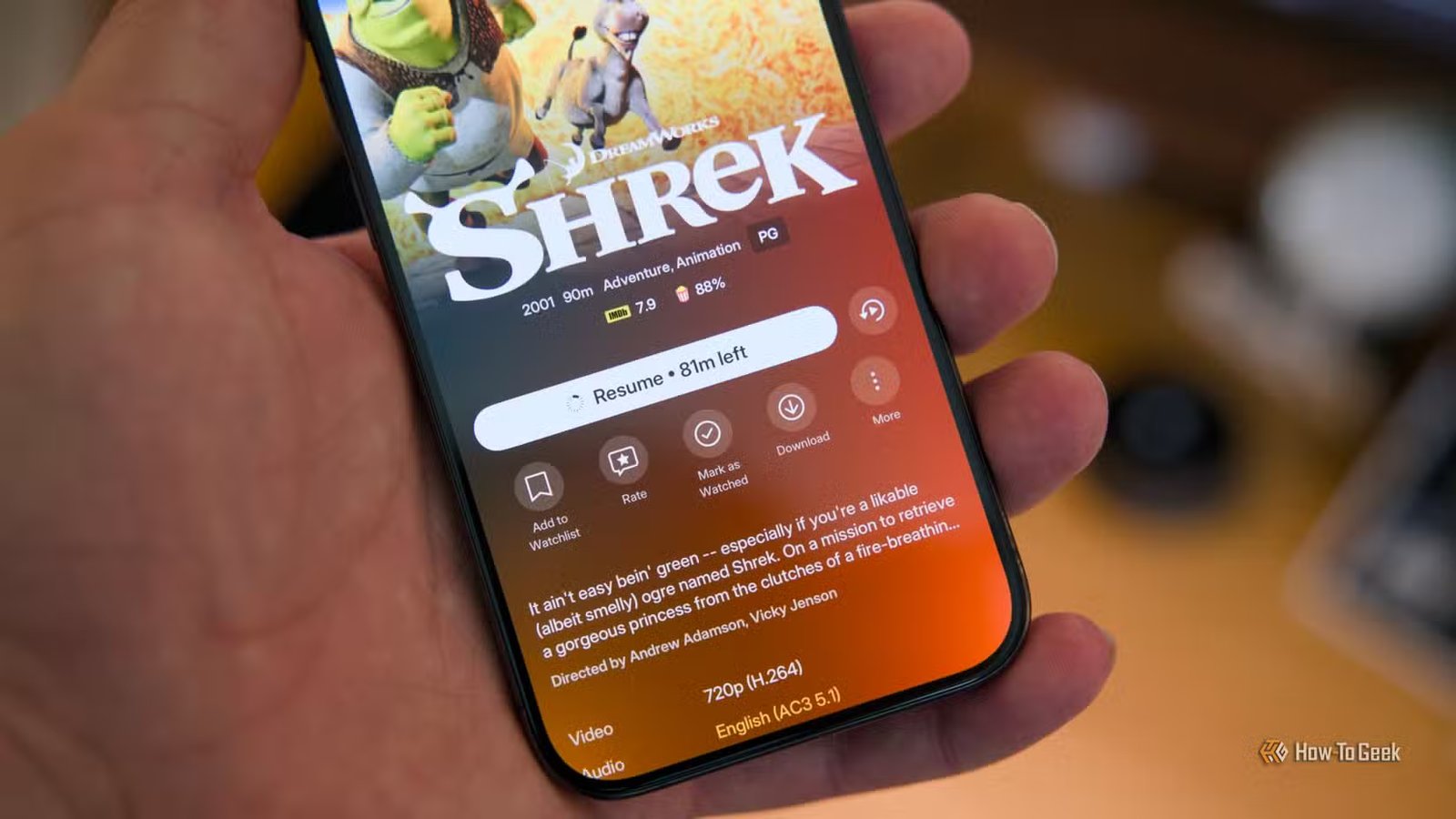 Un iPhone 15 Pro tenu dans une main montrant l'application mobile Plex avec l'icône de téléchargement visible sur le film Shrek.