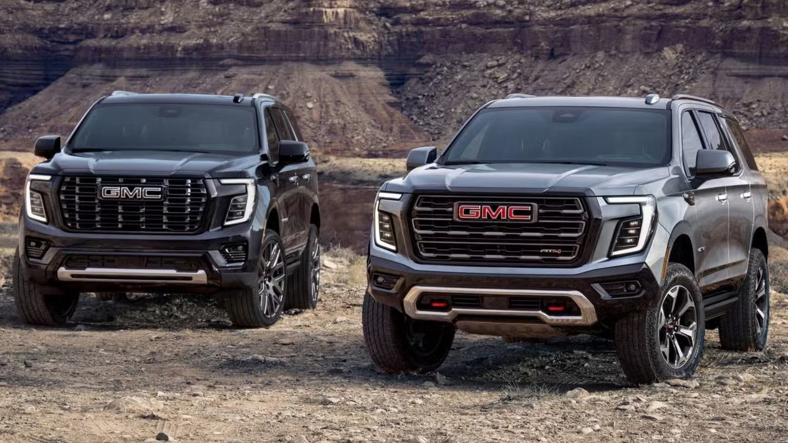 Plan statique 3/4 avant d'un GMC Yukon Denali 2025 noir aux côtés d'un GMC Yukon AT4 2025 gris.