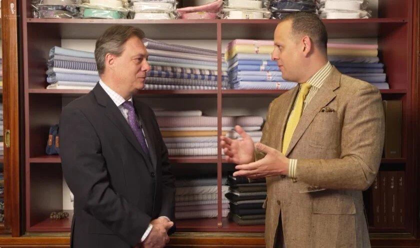 Sven Raphael Schneider portant un manteau de sport en lin marron tabac et une cravate en tricot jaune discutant avec le maître tailleur Robert Ruzicka dans la boutique historique du Zum Jockey Club à Vienne.