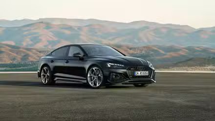 Vue complète d'une Audi RS5 Sportback noire garée sur le tarmac avec des montagnes en arrière-plan.