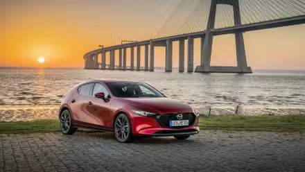 Plan 3/4 avant d'une Mazda 3 2019 garée devant un pont