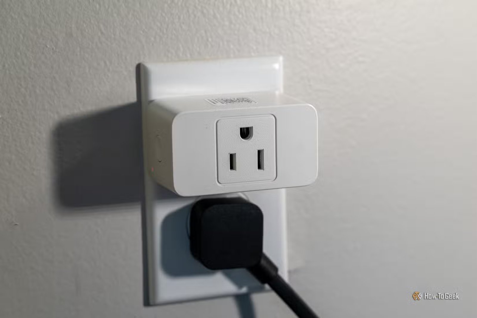 Prise intelligente de surveillance de l'énergie meross MSS315 installée dans une prise murale au-dessus d'un adaptateur secteur.